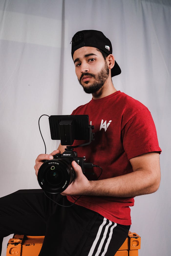 Young male videographer holding camera indoors, showcasing his professional equipment.