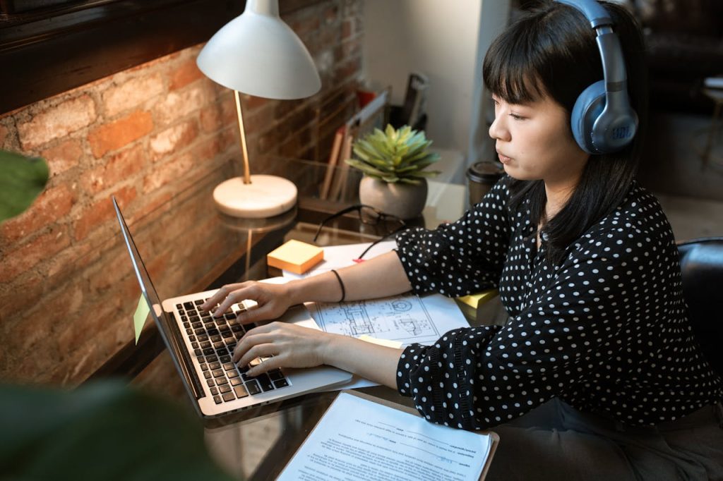 woman-in-black-and-white-polka-dot-long-sleeve-shirt-using-macbook-air-5921786 Focused woman wearing headphones, working on a laptop in a cozy home office setup with natural light.